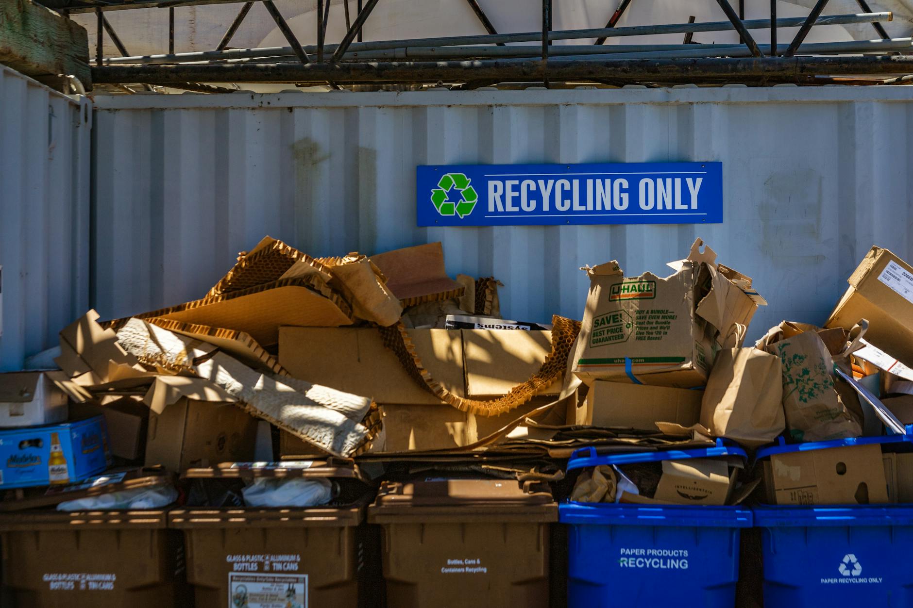 Recycling bins overflowing with cardboard & a sign that says, "Recycling only."