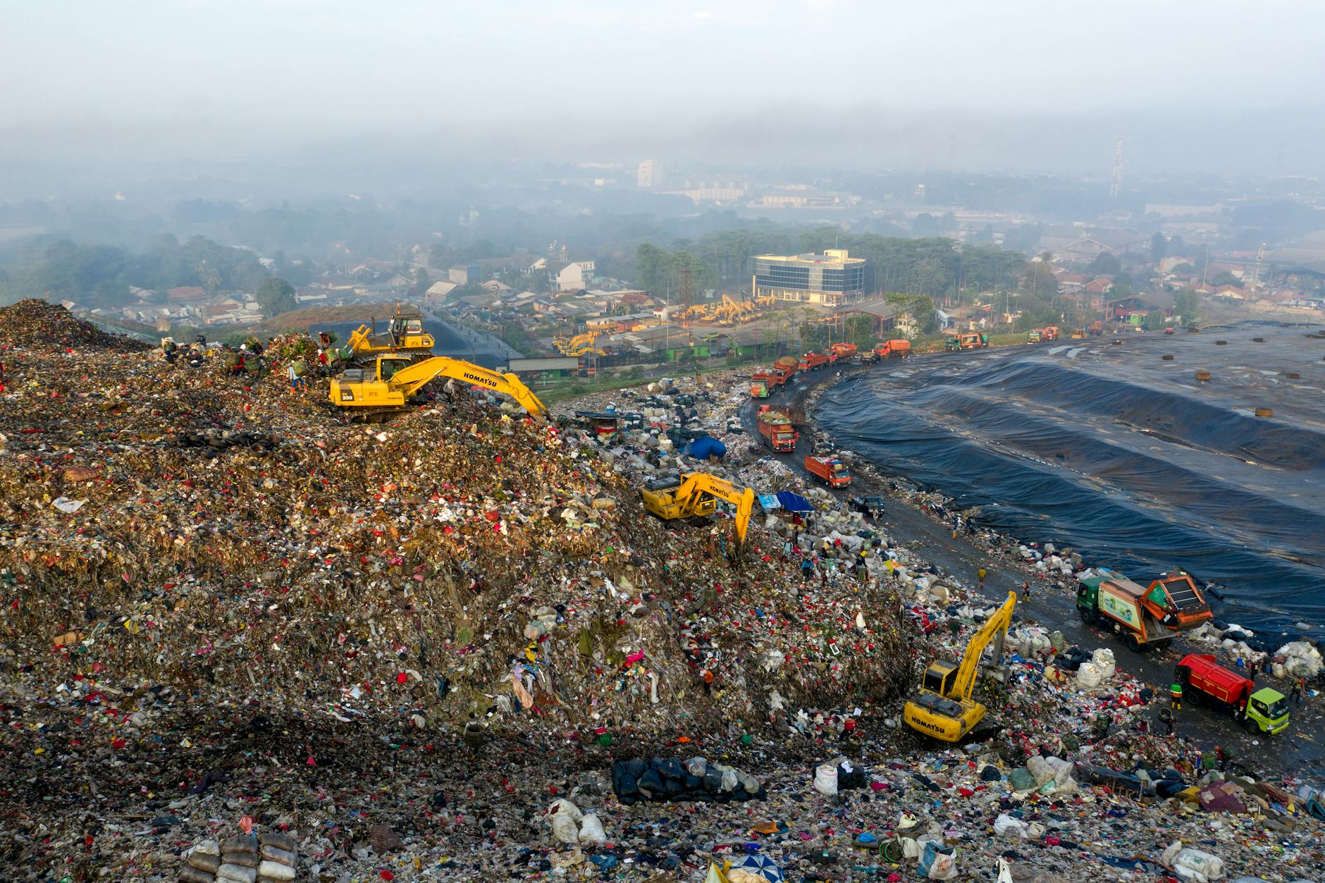 A distant view of a large landfill with many trucks working with the piles of trash.