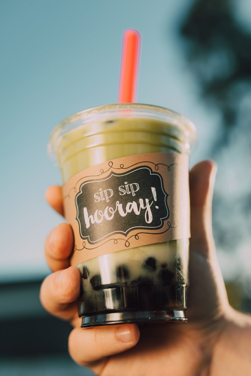A hand holding a boba tea with a paper wrap that says, "Sip Sip Hooray!"