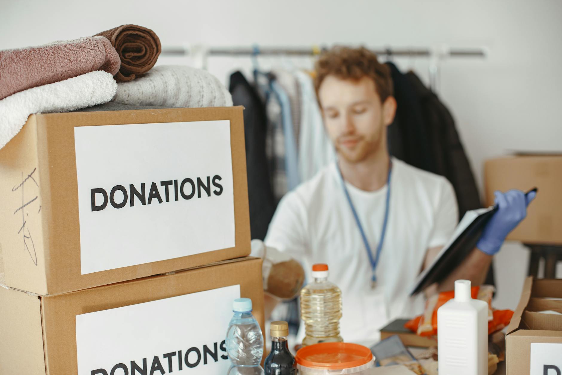 Donations on a table with boxes and clothing surrounding. A volunteer is working to organize the donations.